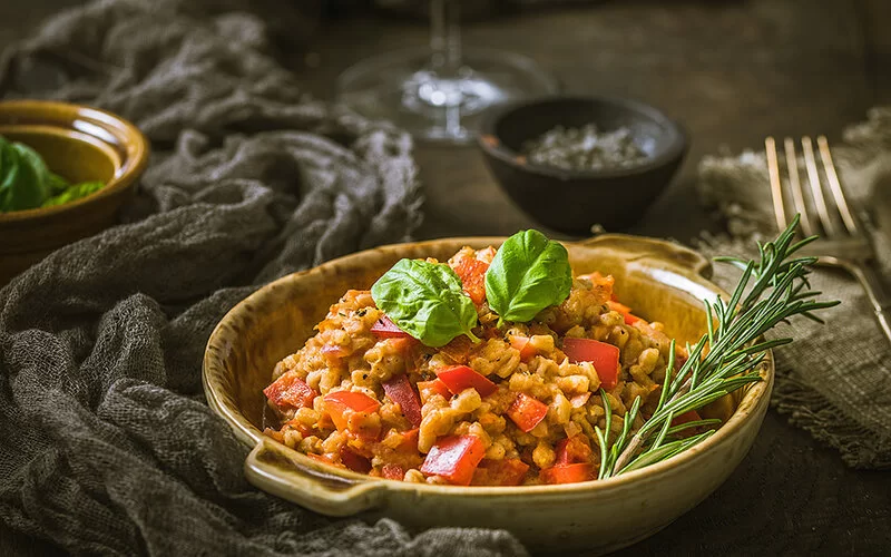 Auf einem Tisch steht eine Schale mit hausgemachten Dinkel-Risotto mit Tomaten und roter Paprika.