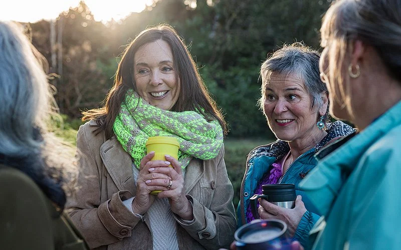 Eine Gruppe von Frauen mit einem Getränk in der Hand unterhält sich in der Natur.