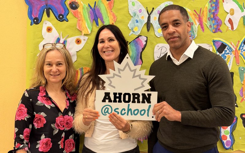 Vertreterinnen und Vertreter des Projekts Ahorn@school präsentieren das Bewegungs- und Gesundheitsprogramm für Schulen vor einer bunten Schmetterlingswand.