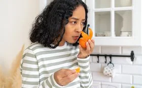 Eine Frau steht in einer Küche und riecht mit ernster Miene an einer Mandarine.