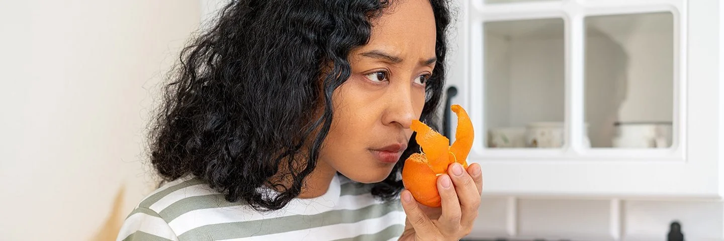 Eine Frau steht in einer Küche und riecht mit ernster Miene an einer Mandarine.