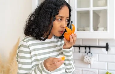 Eine Frau steht in einer Küche und riecht mit ernster Miene an einer Mandarine.