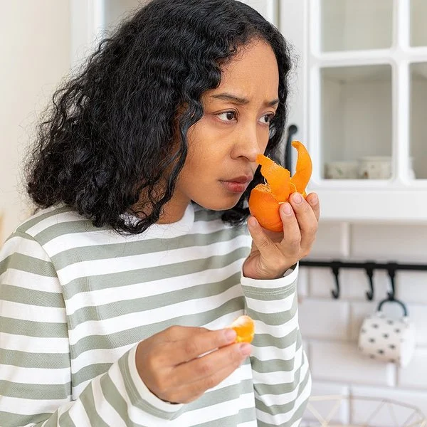 Eine Frau steht in einer Küche und riecht mit ernster Miene an einer Mandarine.