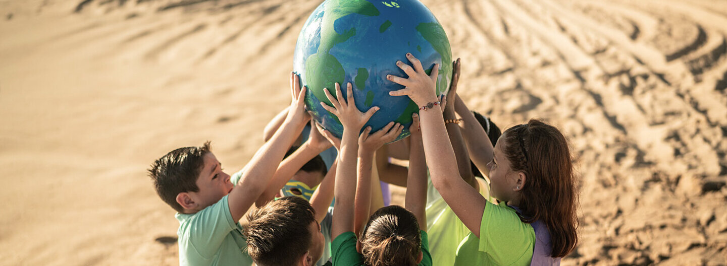 Eine Gruppe von Kindern steht am Strand und hält einen Erdball in den Händen.