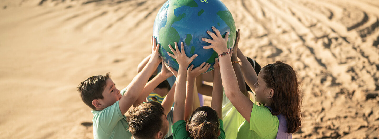 Eine Gruppe von Kindern steht am Strand und hält einen Erdball in den Händen.