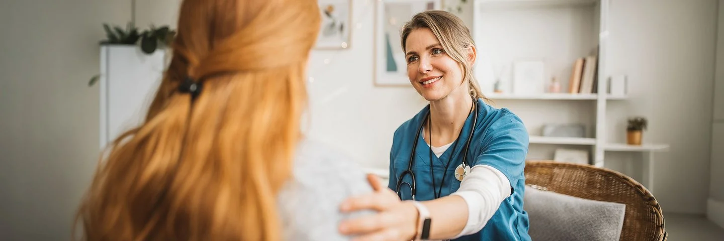 Pflegekraft und Frau sitzen sich gegenüber und schauen sich an.