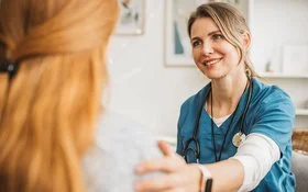 Pflegekraft und Frau sitzen sich gegenüber und schauen sich an.