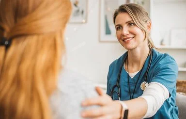 Pflegekraft und Frau sitzen sich gegenüber und schauen sich an.