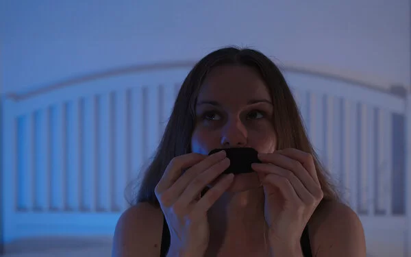 Eine junge Frau sitzt auf ihrem Bett und klebt sich ein Pflaster auf den Mund.
