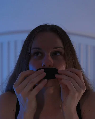 Eine junge Frau sitzt auf ihrem Bett und klebt sich ein Pflaster auf den Mund.
