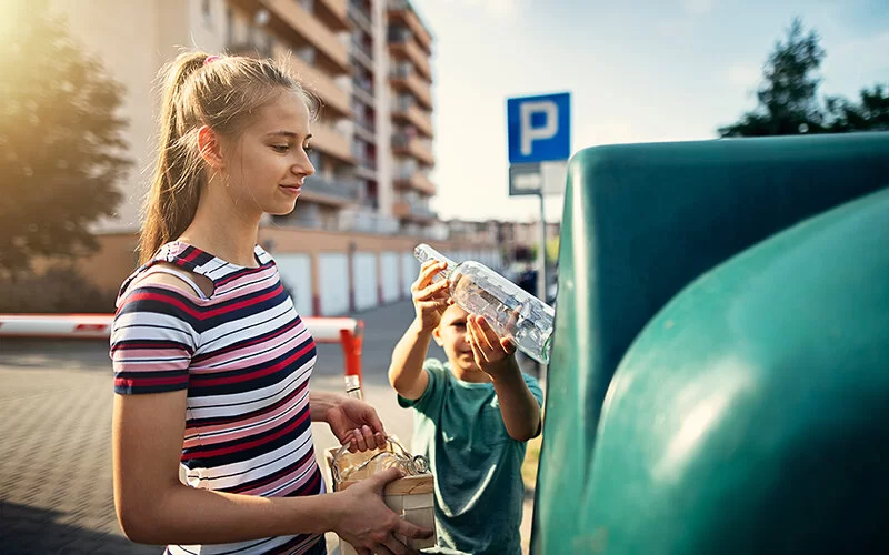 Bruder und Schwester werfen Glasflaschen in einen Glascontainer.