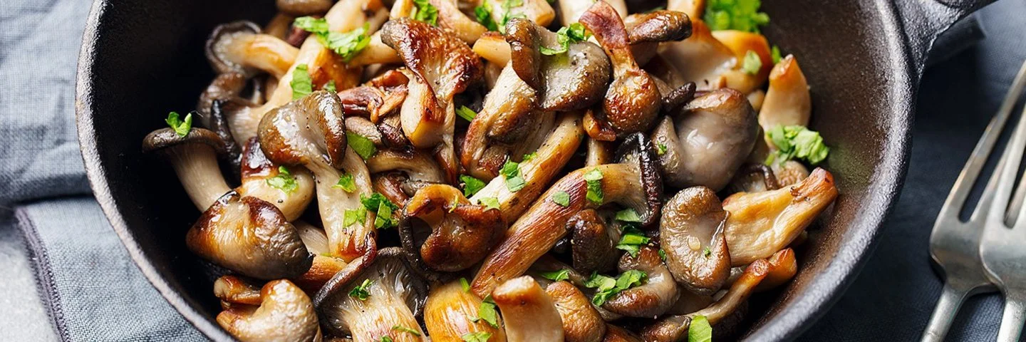 Gebratene braune Pilze mit Kräutern in einer gusseinernen Pfanne.