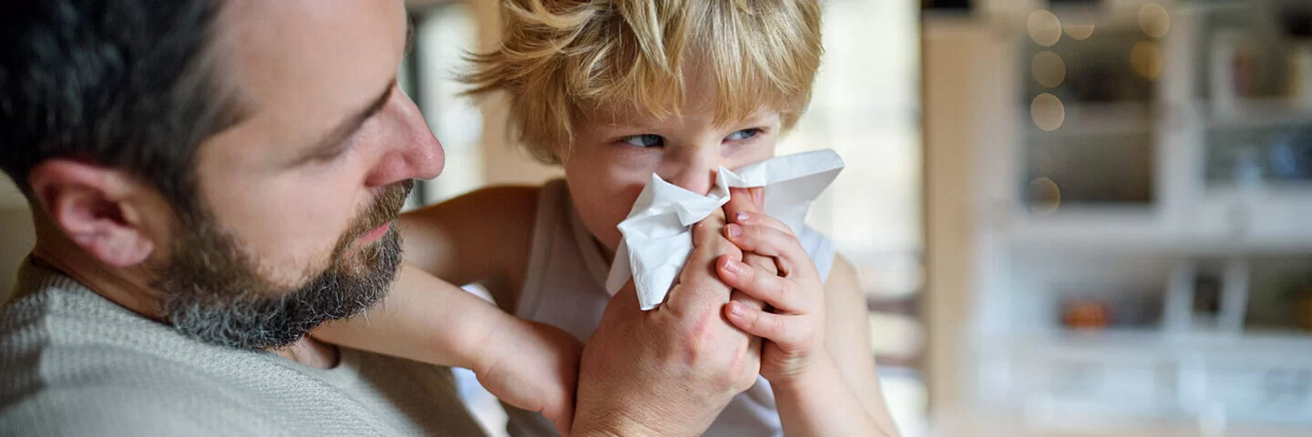 Vater hält seinen am RS-Virus erkrankten Sohn im Arm und putzt ihm die Nase.