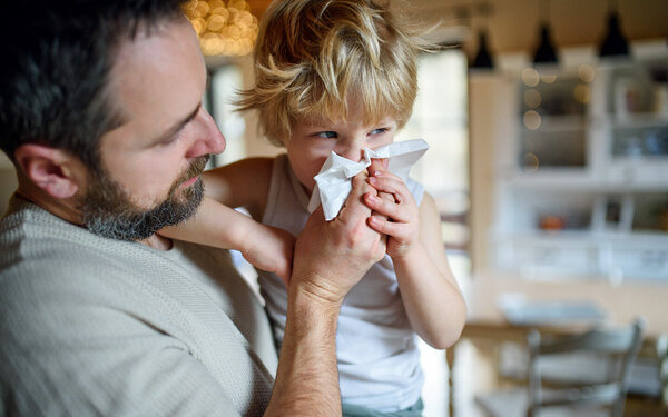 Vater hält seinen am RS-Virus erkrankten Sohn im Arm und putzt ihm die Nase.