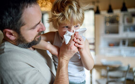 Vater hält seinen am RS-Virus erkrankten Sohn im Arm und putzt ihm die Nase.
