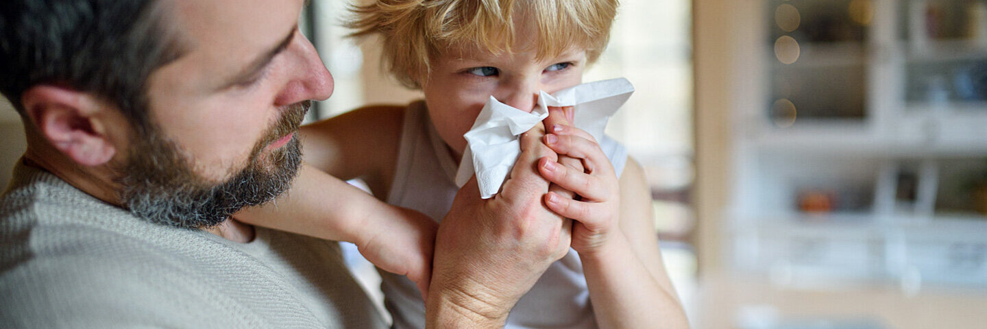 Vater hält seinen am RS-Virus erkrankten Sohn im Arm und putzt ihm die Nase.