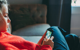 Ein junges Mädchen in einem roten Pullover schaut auf ihr Smartphone.