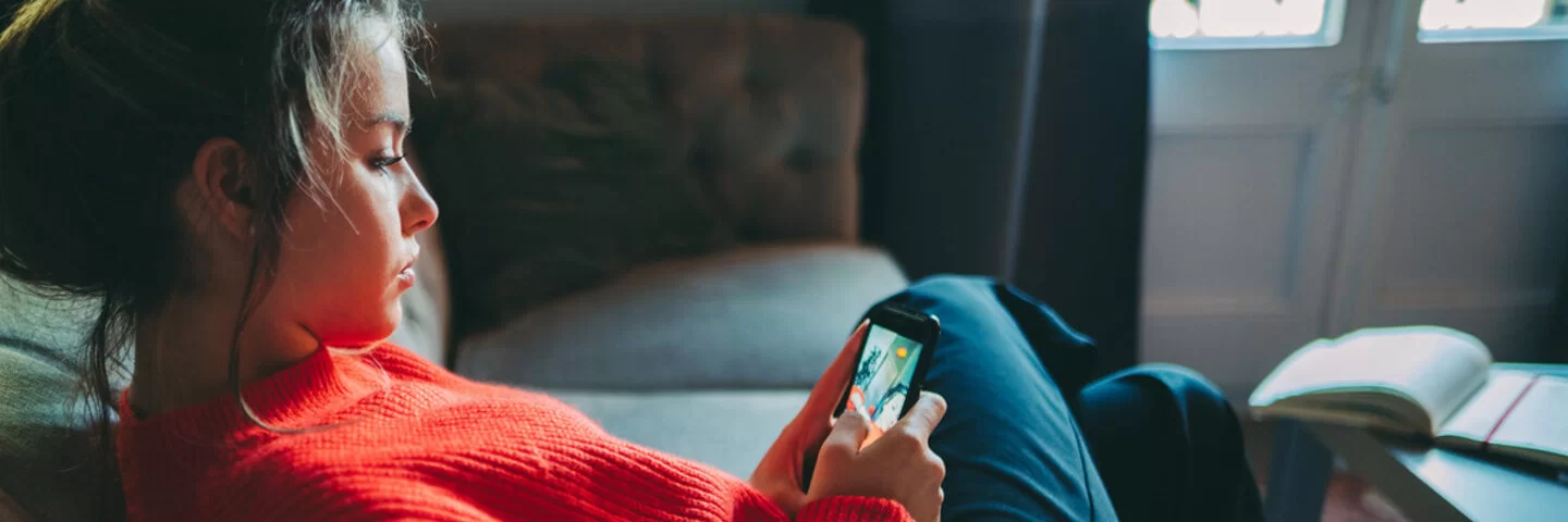 Ein junges Mädchen in einem roten Pullover schaut auf ihr Smartphone.