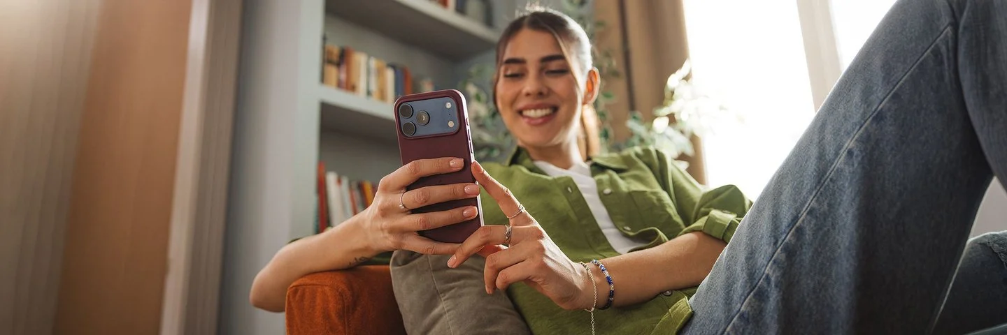 Junge, erwachsene Frau sitzt auf dem Sofa und hält ein Smartphone in der Hand. Sie nutzt ihr Handy zur digitalen Identifikation für die ePA.