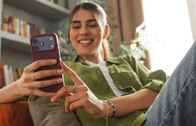 Junge, erwachsene Frau sitzt auf dem Sofa und hält ein Smartphone in der Hand. Sie nutzt ihr Handy zur digitalen Identifikation für die ePA.