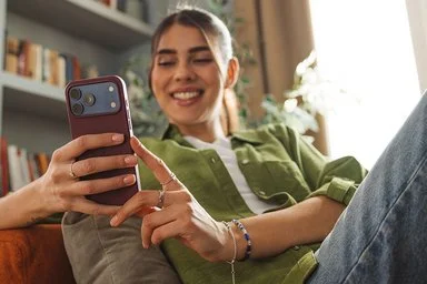 Junge, erwachsene Frau sitzt auf dem Sofa und hält ein Smartphone in der Hand. Sie nutzt ihr Handy zur digitalen Identifikation für die ePA.