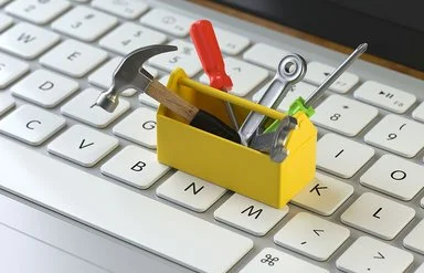 Eine kleine gelbe Werkzeugkiste mit Werkzeug steht auf einer Computertastatur.