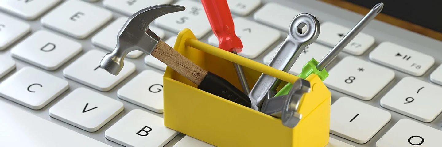 Eine kleine gelbe Werkzeugkiste mit Werkzeug steht auf einer Computertastatur.