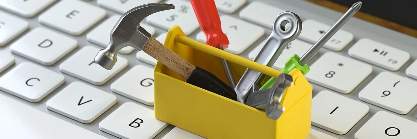 Eine kleine gelbe Werkzeugkiste mit Werkzeug steht auf einer Computertastatur.