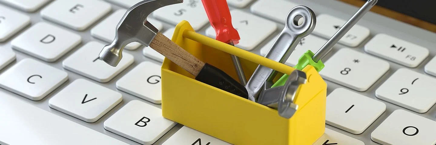 Eine kleine gelbe Werkzeugkiste mit Werkzeug steht auf einer Computertastatur.