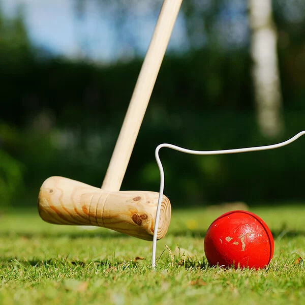 Ein Krocket-Spielfeld auf einem gepflegten Rasen. Zu sehen sind Krocket-Schläger, Kugel und Tor.