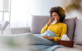 Frau mit Erkältung oder Grippe sitzt auf der Couch im Wohnzimmer.