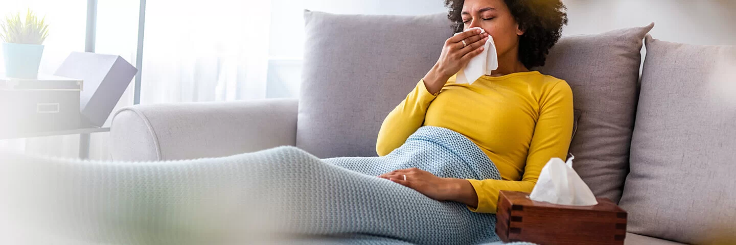 Frau mit Erkältung oder Grippe sitzt auf der Couch im Wohnzimmer.