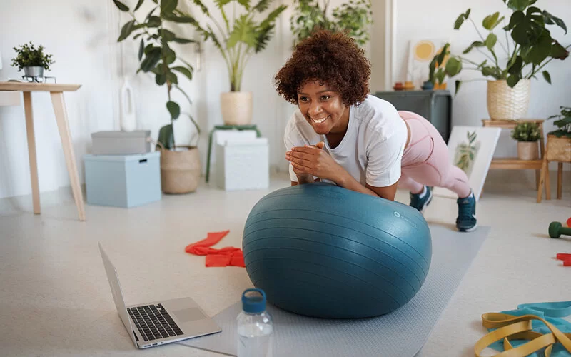 Eine junge Frau plankt auf einem Gymnastikball, dabei stützt sich sie mit den Ellenbogen auf den Ball, die Füße sind auf der Trainingsmatte.