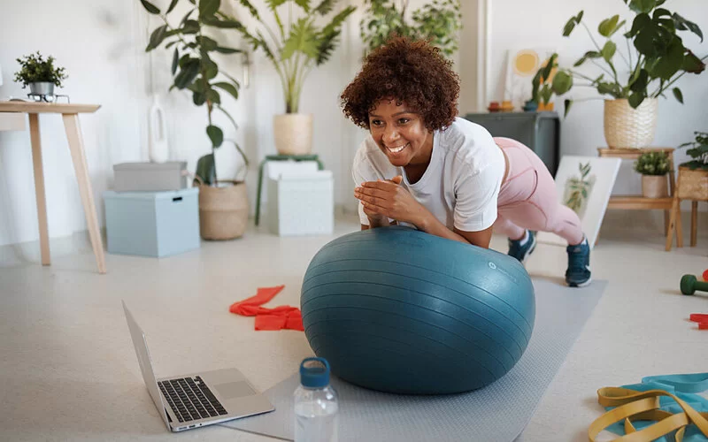Eine junge Frau plankt auf einem Gymnastikball, dabei stützt sich sie mit den Ellenbogen auf den Ball, die Füße sind auf der Trainingsmatte.