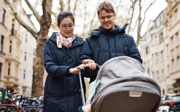 Ein junges Paar geht in der Stadt mit einem Kinderwagen kurz nach der Geburt spazieren.