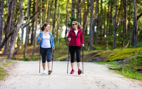 Zwei Frauen beim Nordic Walking im Wald mit Trekkingstöcken.