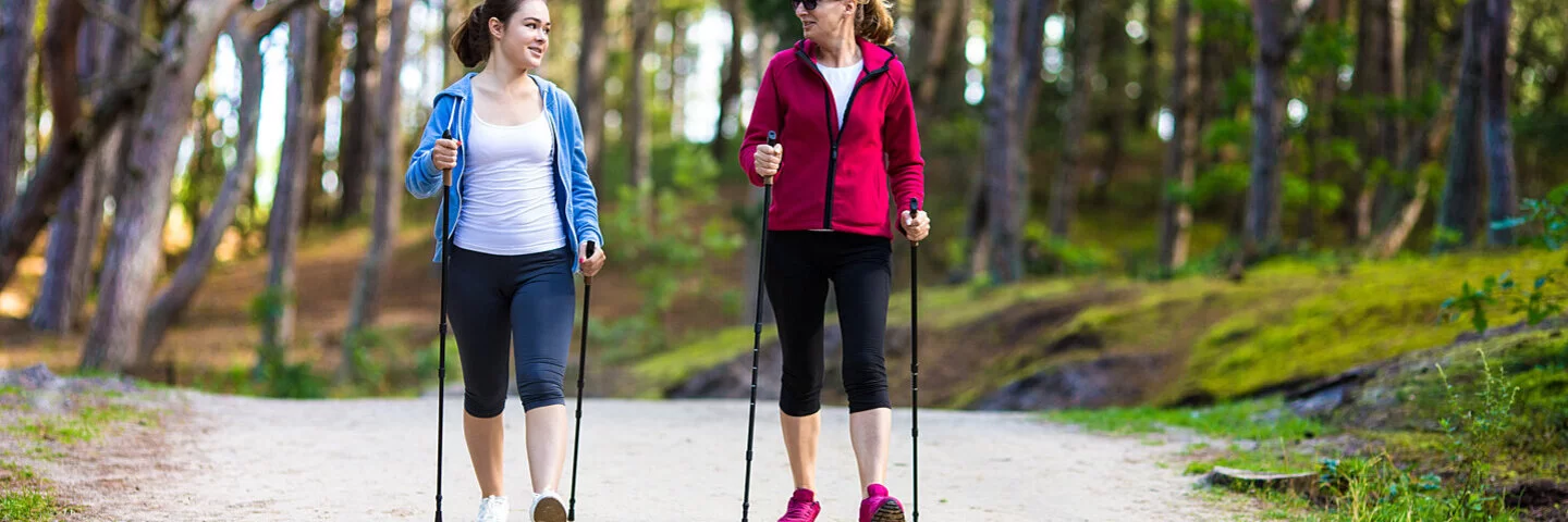 Zwei Frauen beim Nordic Walking im Wald mit Trekkingstöcken.