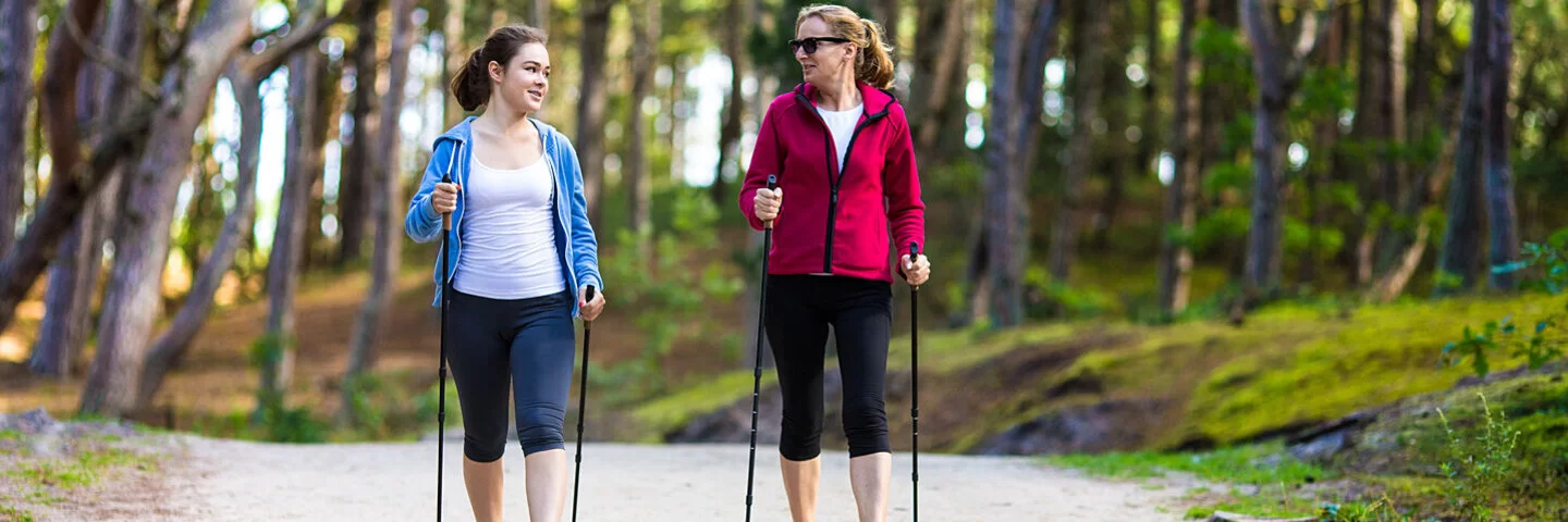 Zwei Frauen beim Nordic Walking im Wald mit Trekkingstöcken.