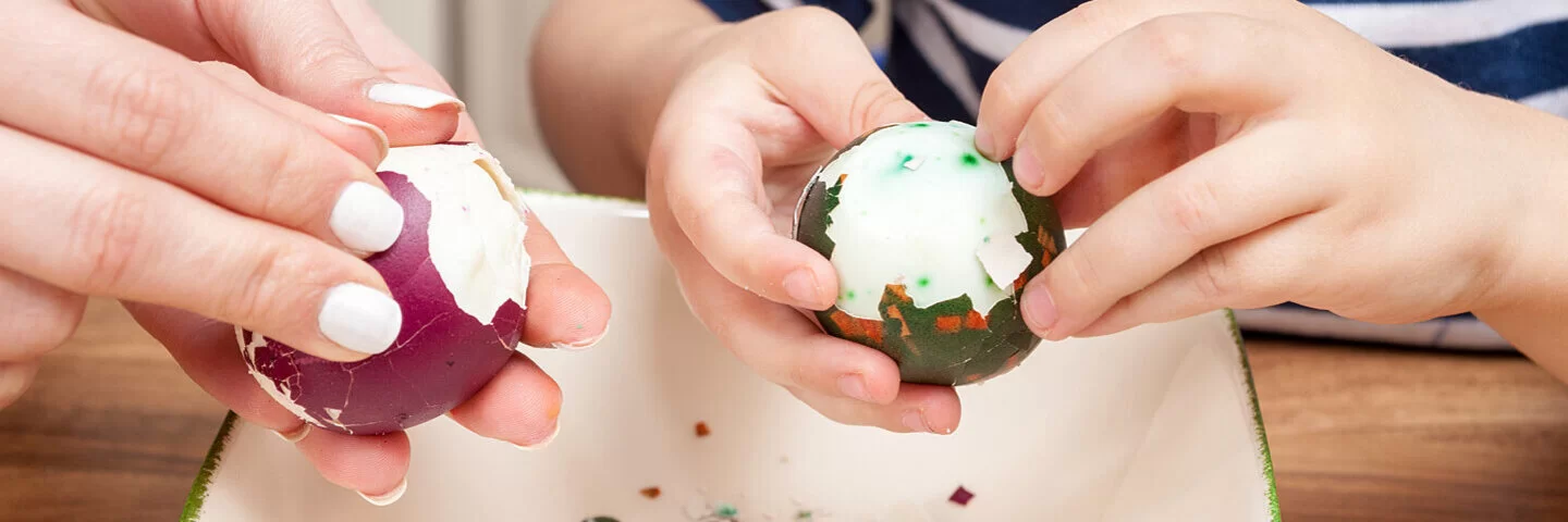 Mutter und Kind pellen übriggebliebene Ostereier für neue Eier-Rezepte.