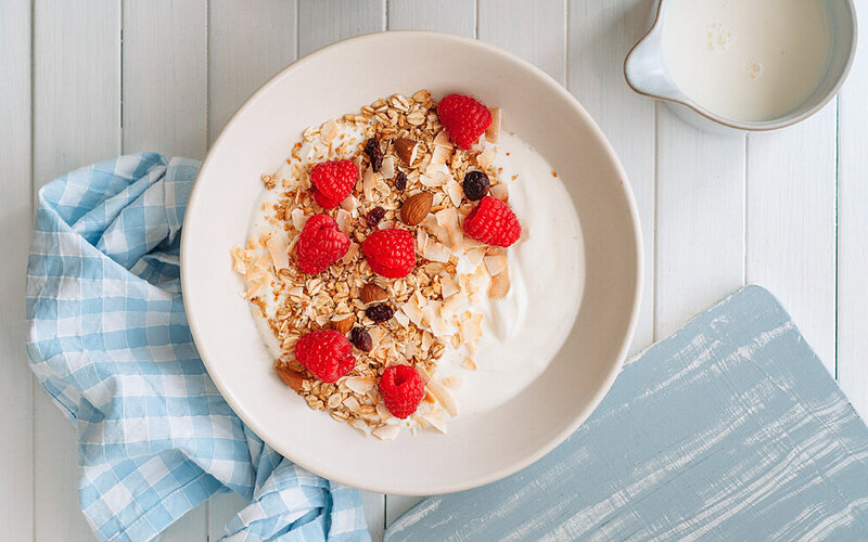 Joghurt mit Himbeeren, Nüssen und Haferflocken in einer Schale.