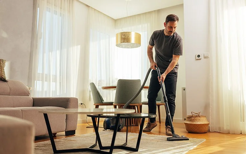 Mann im mittleren Alter saugt den Wohnzimmerteppich.