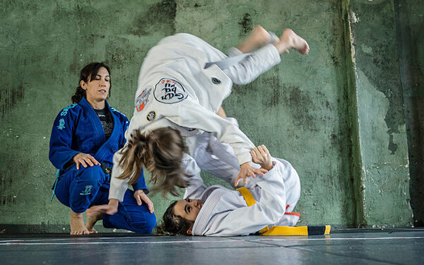 Zwei Mädchen kämpfen miteinander, die Trainerin begleitet den Kampf.