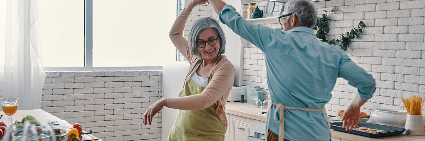 Ein Seniorenpaar tanzt in der Küche miteinander. 