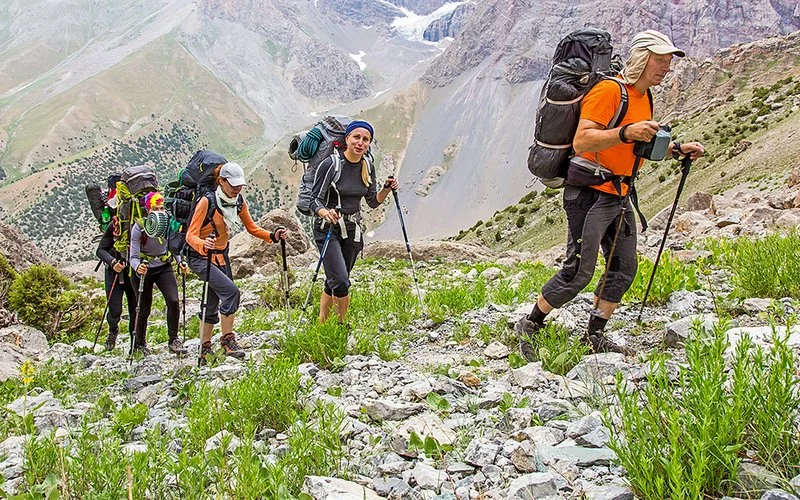 Eine kleine Gruppe wird von einem Bergführer auf einen Gipfel geführt. Im Hintergrund ist ein Gletscher zu sehen.
