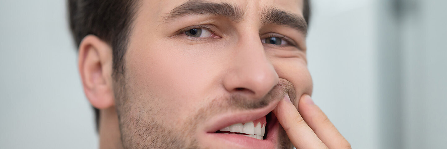 Ein junger Mann schaut kritisch in den Spiegel, schiebt mit der linken Hand die Lippe etwas hoch und schaut, ob er eine Zahnfleischentzündung hat.