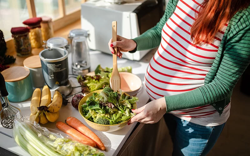 Eine Schwangere bereitet sich einen frischen Salat zu.
