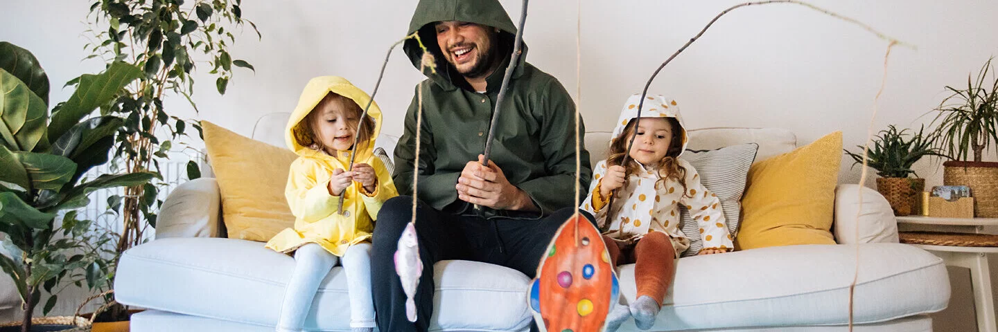 Vater spielt mit seiner Tochter und ihrer Freundin im Wohnzimmer, so hilft er, die Kinderfreundschaft aufzubauen.