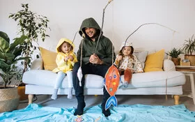 Vater spielt mit seiner Tochter und ihrer Freundin im Wohnzimmer, so hilft er, die Kinderfreundschaft aufzubauen.