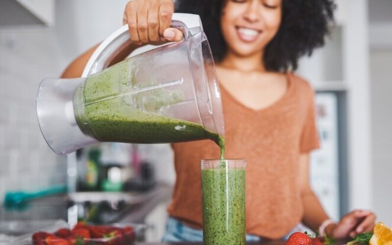 Eine Frau schenkt einen selbst gemachten grünen Smoothie vom Mixer in ein Glas.