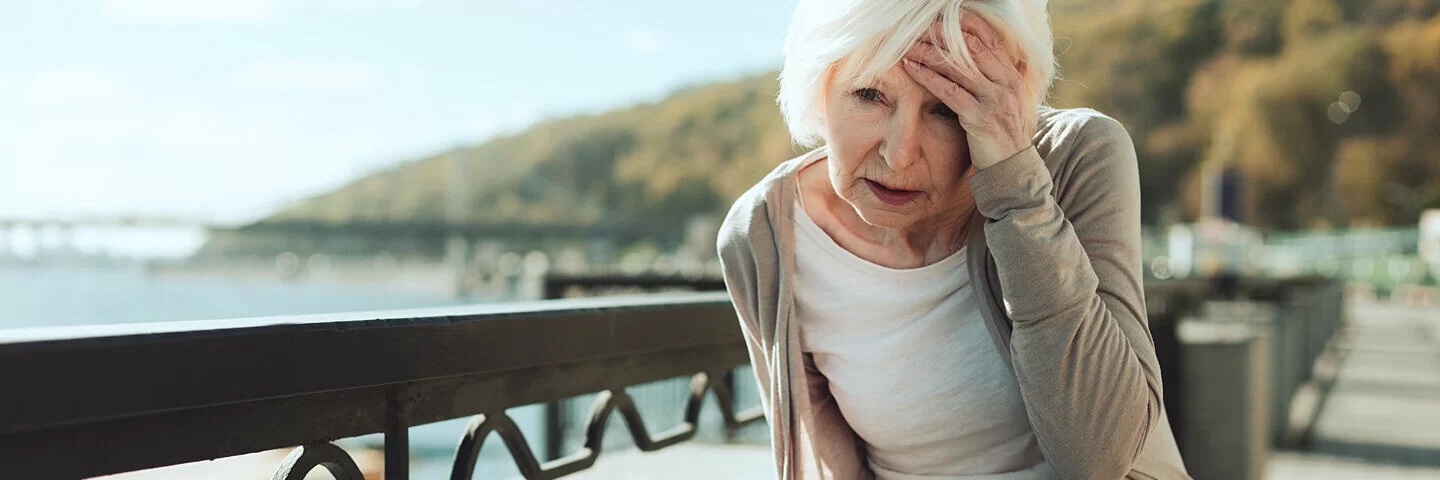 Einer Dame ist schwindelig und sie muss sich an einer Brüstung festhalten, weil sie einen Schlaganfall hat.